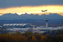 Flughafen München bei Sonnenuntergang mit abhebendem Flugzeug und den Alpen im Hintergrund