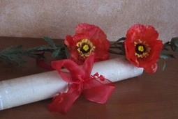 Aufgerollter Gutschein mit roter Schleife und Mohnblumen